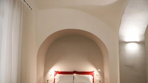 A bedroom with a large arched ceiling, a bed with white linens, red pillows, and two bedside tables with lamps. - Il Loggiato - Stella Apartment by Wonderful Italy (Naples)