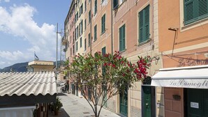 A narrow street with traditional buildings, a tree with red flowers, and a sign for "La Camogli". - Il Mare di Camogli da un Obl by Wonderful Italy (Camogli)