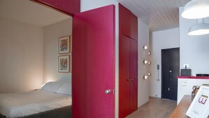 A bedroom with a bed, a red wardrobe, a desk with a computer, and a door with lights. - Il Mare di Camogli da un Obl by Wonderful Italy (Camogli)