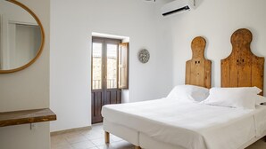 Ein Schlafzimmer mit einem hölzernen Bett, weißer Bettwäsche, einem runden Spiegel und einer Tür, die nach draußen führt.