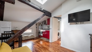 A spacious living area with a wooden staircase, a kitchen with red cabinets, and a flat-screen TV mounted on the wall. - La Mansarda di Via Zamboni by Wonderful Italy (Bologna)