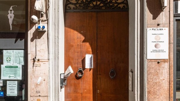 A wooden double door with a metal arch above it, a small table with chairs in front, and a sign on the right side. - La Mansarda di Via Zamboni by Wonderful Italy (Bologna)