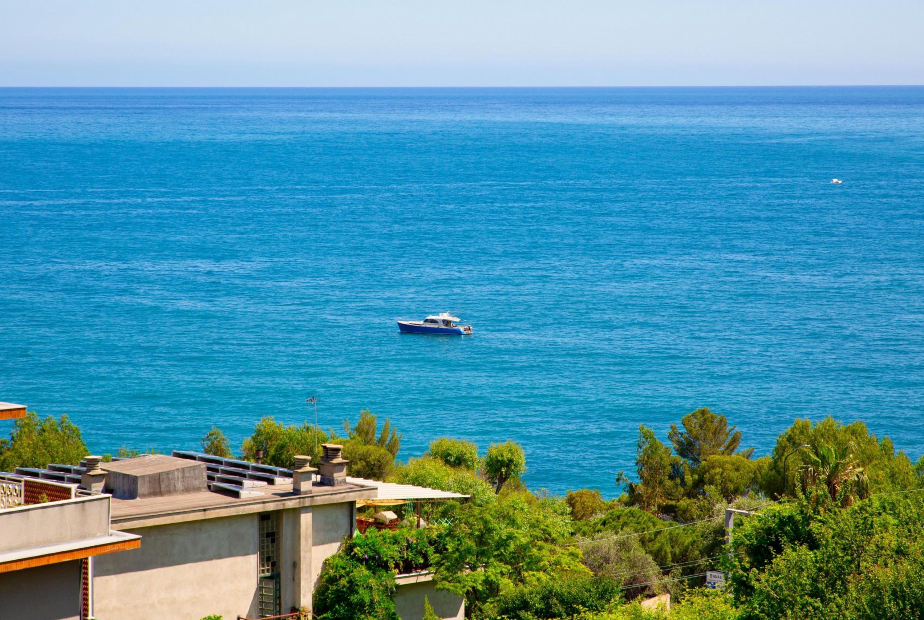 A coastal view with a boat on the water, buildings with balconies, and lush greenery.
