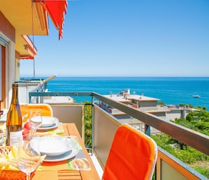 A balcony with a table set for dining, overlooking a coastal view with buildings and the sea. - Le Orchidee 14 con Vista Mare by Wonderful Italy (Sanremo)