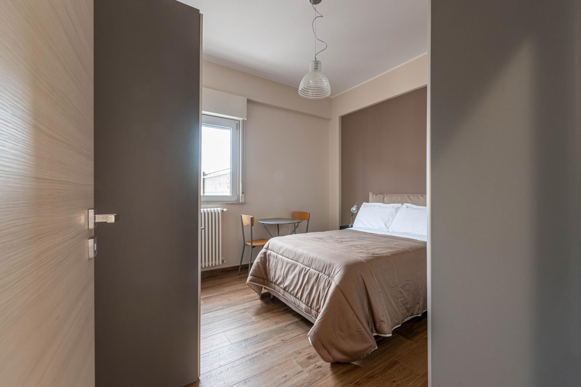 A bedroom with a bed, a chair, a table, and a window.