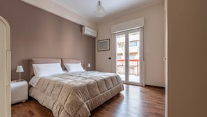 Un dormitorio con una cama grande, una mesita de noche, una lámpara, un equipo de aire acondicionado, un cuadro en la pared y un ventanal corredero al exterior.
