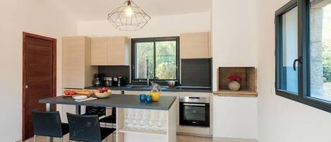 A modern kitchen with a central island, black chairs, and a hanging light fixture.