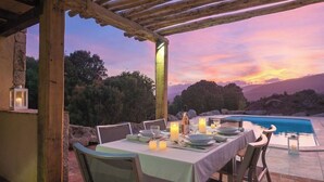Un espace extérieur aménagé pour les repas, avec une piscine, une pergola en bois et une vue sur le coucher de soleil.