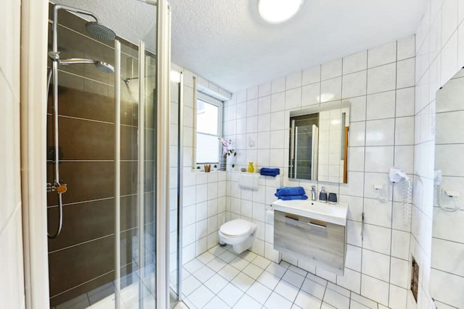 A modern bathroom with a glass-enclosed shower, a toilet, a sink with a mirror, and a tiled floor.