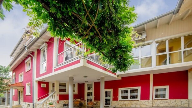 Ein zweistöckiges Gebäude mit roter Fassade, einem Balkon und einem steinernen Fundament.