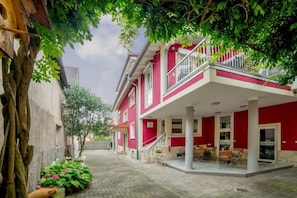 Un bâtiment rouge doté d’un balcon, d’une cour pavée et d’un arbre.