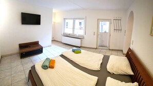 Ein Hotelzimmer mit einem großen Bett, einem an der Wand montierten Fernseher, einem Fenster mit Jalousien und einem Heizkörper.