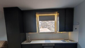 Eine kleine Küche mit dunklen Schränken, einem Fenster und LED-Beleuchtung, einem Spülbecken sowie einem Backofen.
