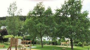 Une aire de jeux avec du sable, des structures en bois et des arbres.