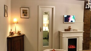 Un salon chaleureux avec une cheminée, un téléviseur fixé au-dessus, et une porte donnant sur une autre pièce.