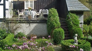 Un espace extérieur abrité, aménagé avec une table et des chaises, entouré de verdure et agrémenté d’une statue.