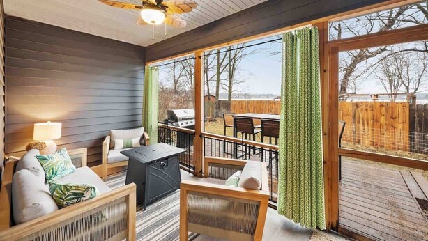 A cozy room with a ceiling fan, large windows, a grill outside, and a view of the backyard.