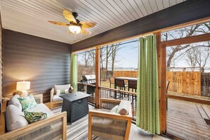 Una habitación acogedora con ventilador de techo, ventanas amplias, una parrilla afuera y vista al patio trasero.