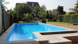 Una piscina rettangolare con bordo piastrellato, circondata da un solarium in mattoni e un basso muretto in pietra.