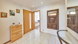 Een gang met een houten dressoir, een deur met een 'HOME' bord en een trap met glazen leuningen.