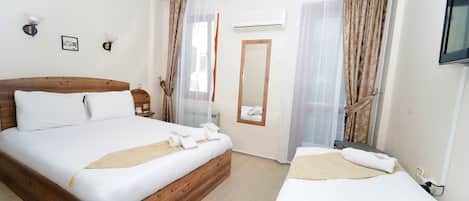 A hotel room with a wooden bed, a smaller bed, a mirror, a TV, and a window with curtains.