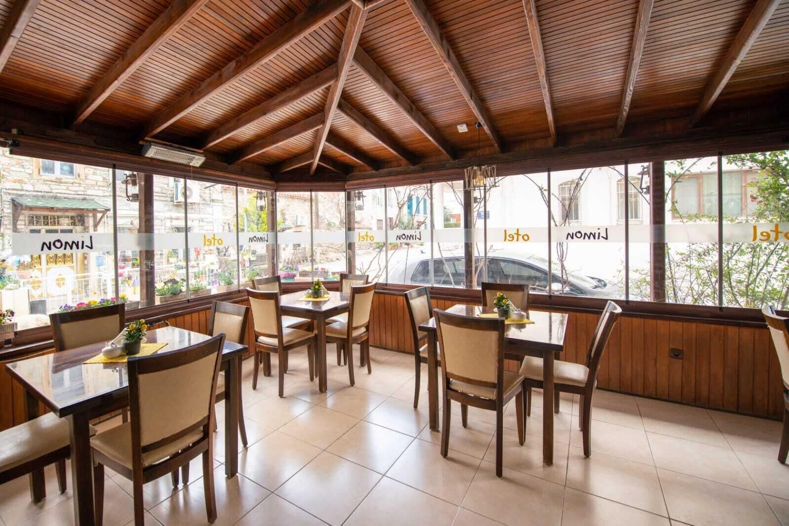 A restaurant with wooden tables and chairs, large windows, and a tiled floor.