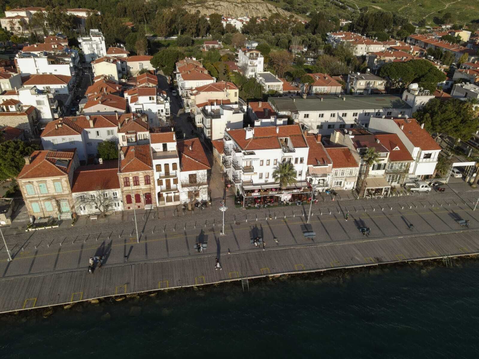 An aerial view of a coastal town with a prominent waterfront promenade, buildings with red-tiled roofs, and a mix of residential and commercial structures.