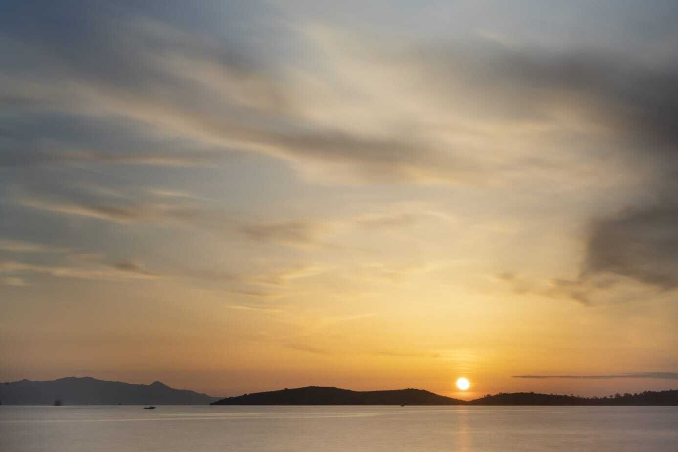 A sunset over a calm body of water with distant landforms.