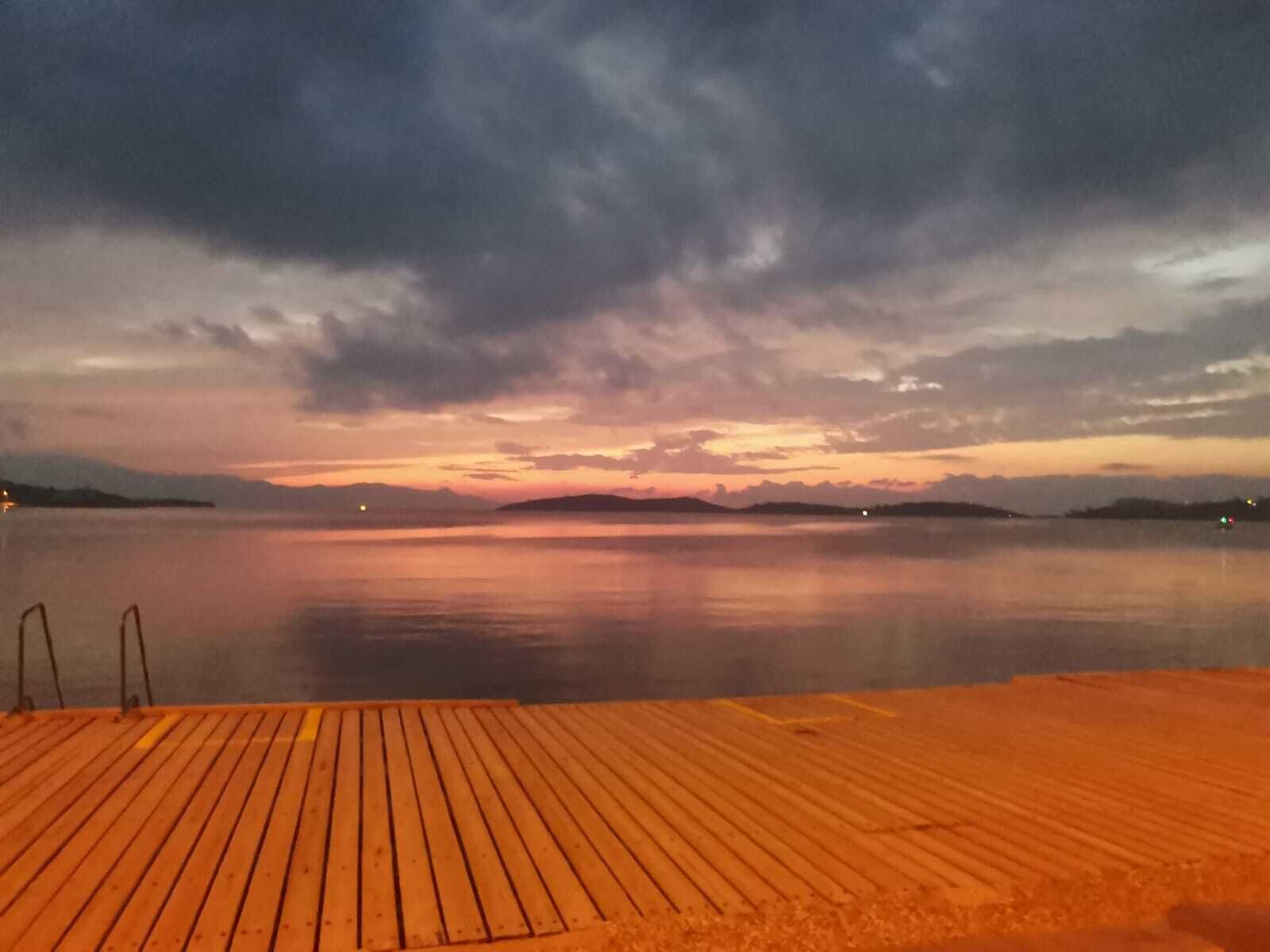 Un muelle de madera que se extiende sobre aguas tranquilas con un atardecer de fondo.