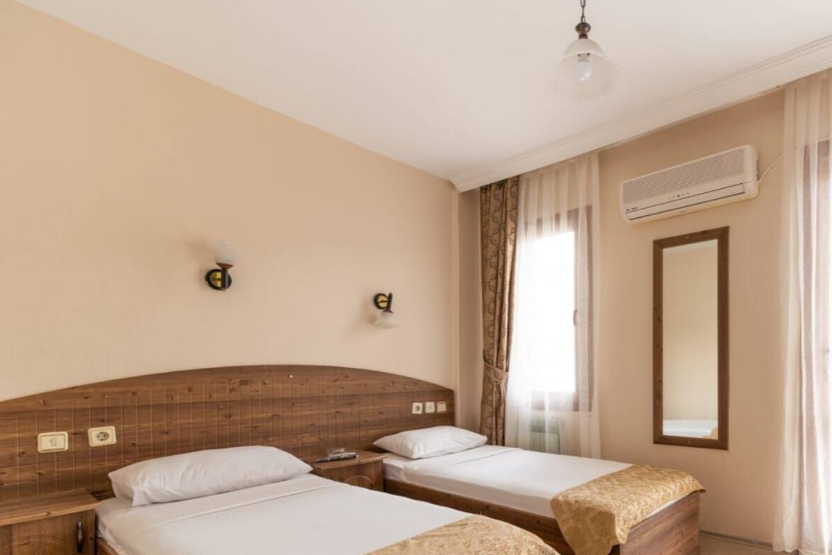 Een hotelkamer met twee houten bedden, een grote spiegel, een airconditioning en een hanglamp.