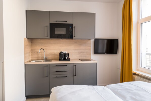 A compact kitchenette with a microwave, coffee maker, and sink, a bed, and a TV mounted on the wall.