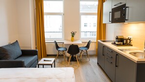 Kompakti hotellihuone, jossa on sänky, sohva, pieni pöytä, ruokailutila kahdella tuolilla, mikroaaltouuni, sekä ikkuna, jossa on verhot.