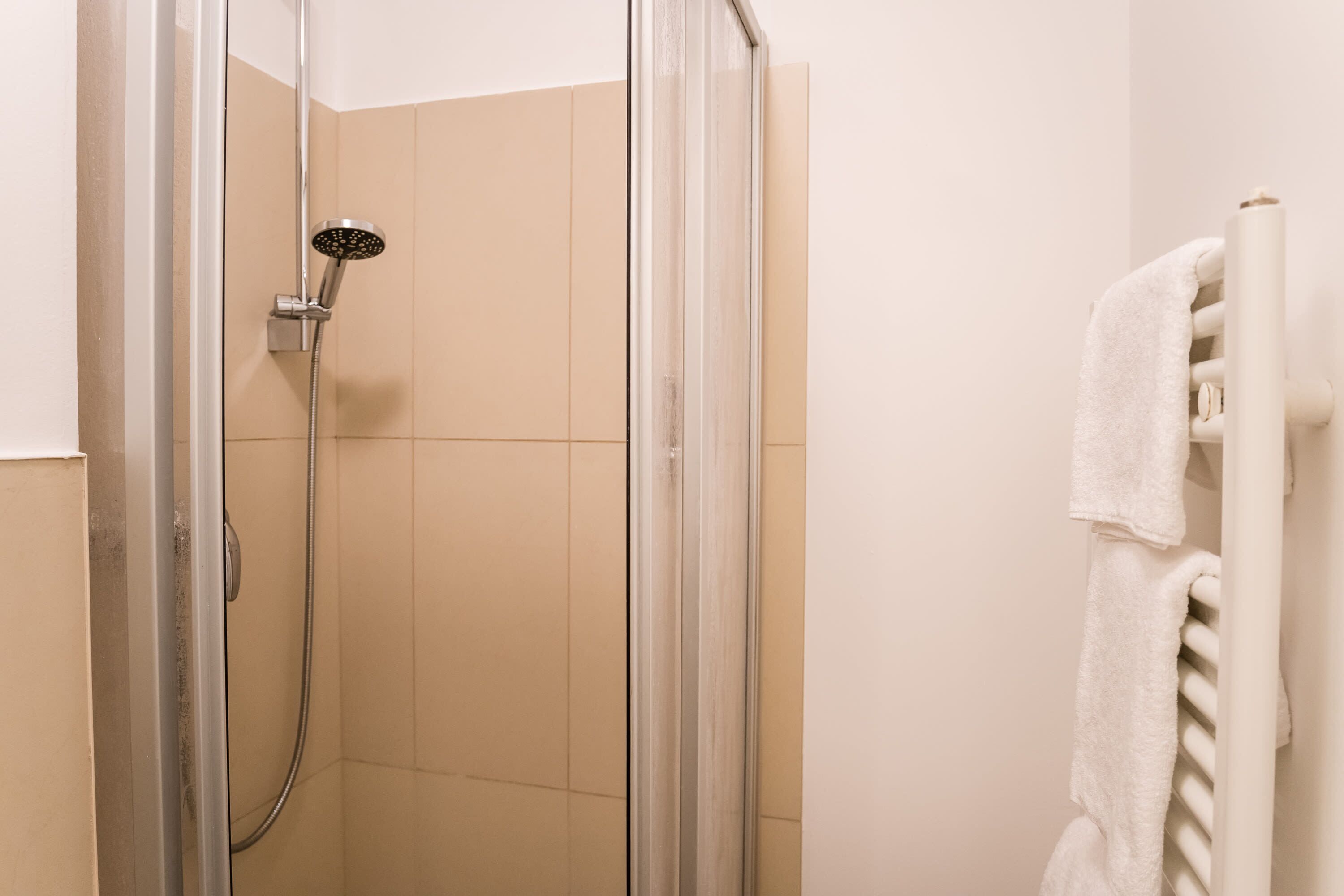 A shower with a glass door, a towel rack with a white towel, and beige tiled walls.
