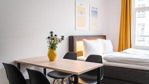 Une chambre d’hôtel comprenant un lit, une table de chevet avec une lampe, une petite table avec des chaises et un vase avec des fleurs.