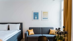 Une chambre d’hôtel moderne, équipée d’un lit, d’un canapé, d’une table à manger et de deux tableaux encadrés accrochés au mur.