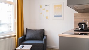 A modern room with a grey sofa, a small wooden table, a kitchen area with a kettle, and two framed pictures of Berlin. - Boxi Studios Berlin S (Berlin)