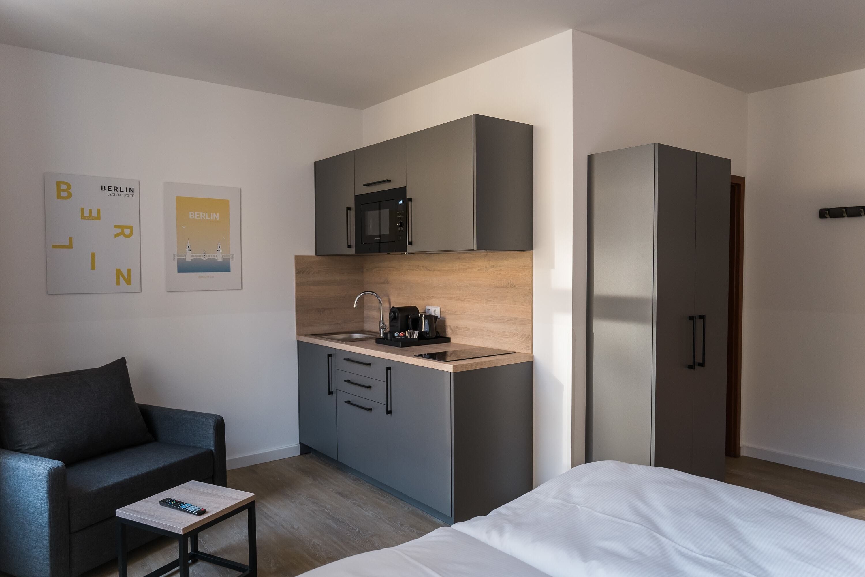 A modern hotel room with a kitchenette, a sofa, a bed, and a small table with a remote control.