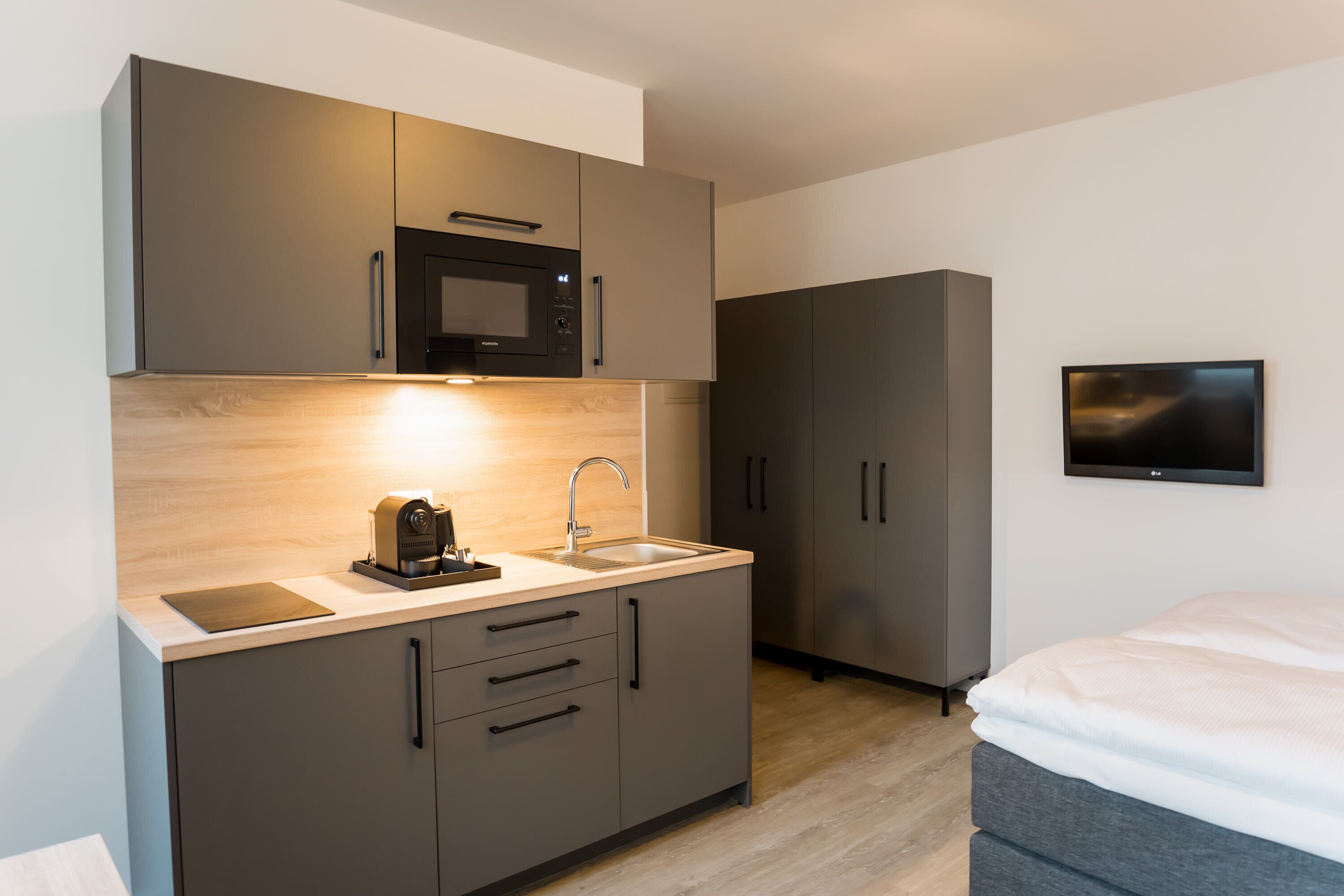A modern kitchen with a microwave, sink, and cabinets, and a TV mounted on the wall.