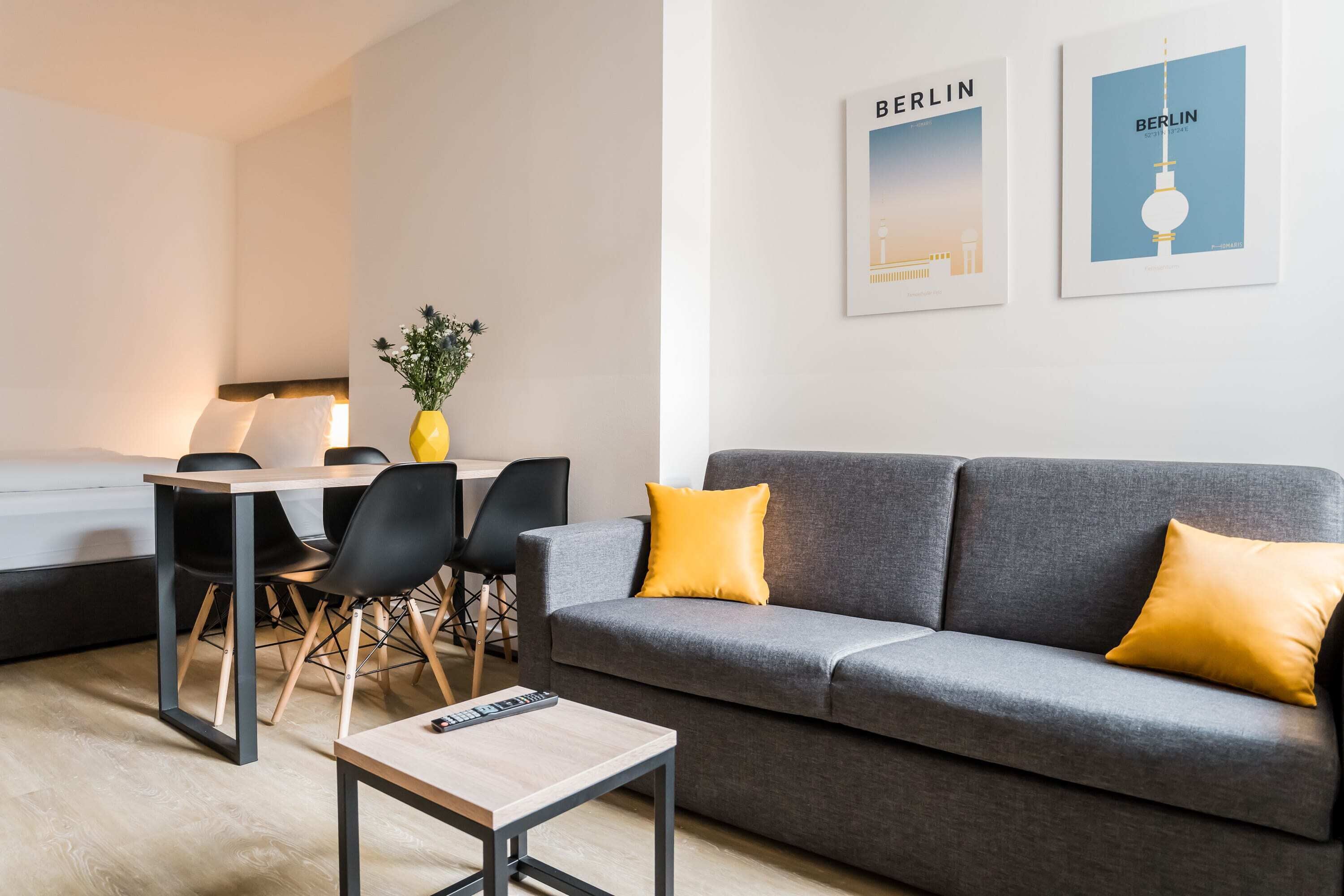 A modern living room with a grey sofa, yellow cushions, a small wooden table, and a dining area with a table and chairs.