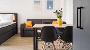 Ein modernes Hotelzimmer mit einem Bett, einer Couch, einem Esstisch mit Stühlen und zwei gerahmten Bildern an der Wand.