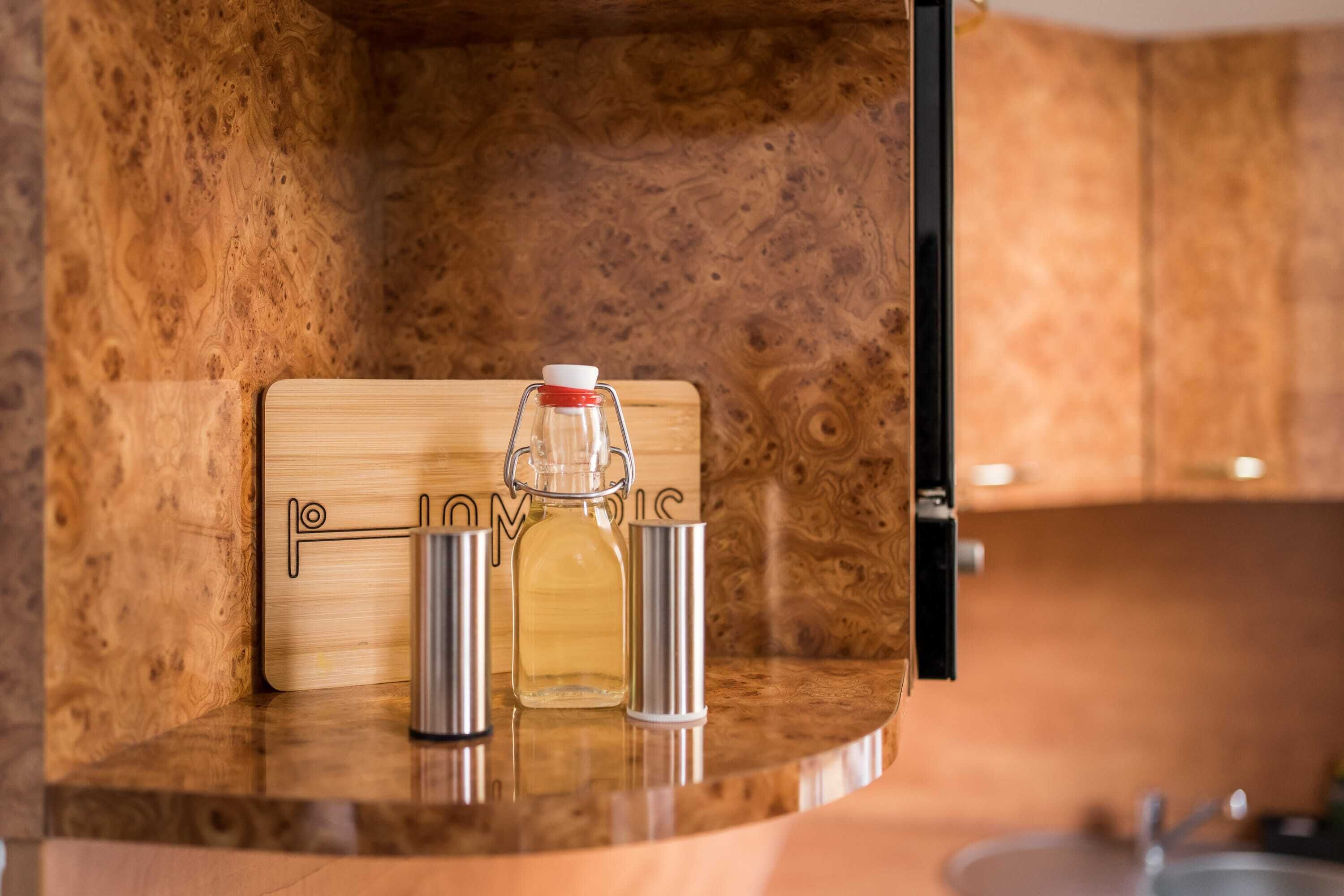 Ein Holzkabinett mit einer Flasche und zwei Metallbechern auf einer Arbeitsplatte.