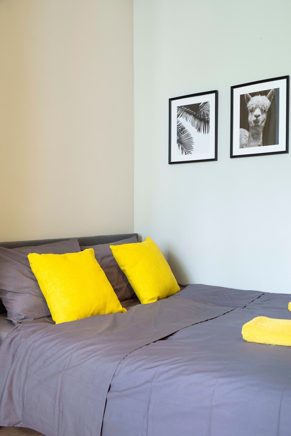 A bed with grey bedding and two bright yellow pillows. There are two framed pictures on the wall above the bed.