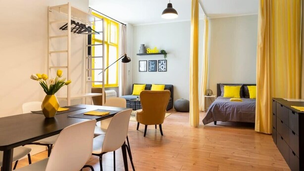 A modern room with a dining area, a bed with yellow curtains, and a small seating area. - Great Apartment close to Kudamm (Berlin)
