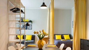 A modern room with a dining table, chairs, a sofa, and a bed. There is a ladder with clothes, a vase with flowers, and a pendant light. - Great Apartment close to Kudamm (Berlin)