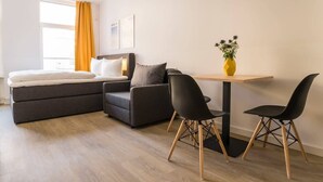 A modern hotel room with a bed, sofa, and a small dining table with chairs.