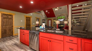 A kitchen with red cabinets, a stainless steel dishwasher, and a granite countertop. - Southern Comfort (Gatlinburg)