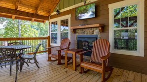 A wooden deck with Adirondack chairs, a table, and a fireplace. - Southern Comfort (Gatlinburg)