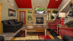 A living room with a stone fireplace, red walls, a black leather sofa, and a red armchair. - Southern Comfort (Gatlinburg)