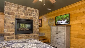 A room with a stone fireplace, a television mounted on the wall, and a wooden cabinet. - Southern Comfort (Gatlinburg)