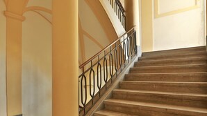 A grand staircase with a metal railing, marble steps, and a columned wall.